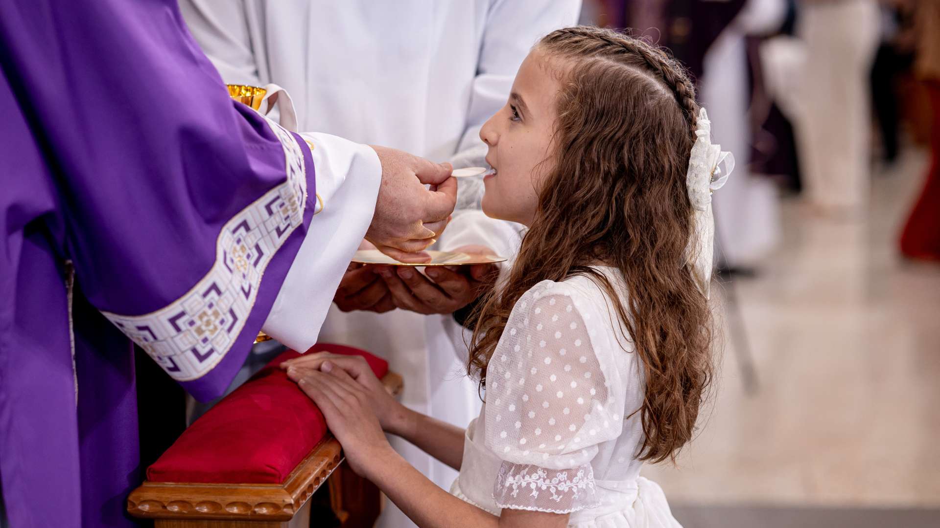 criança rebendo primeira eucaristia das mãos do sacerdote
