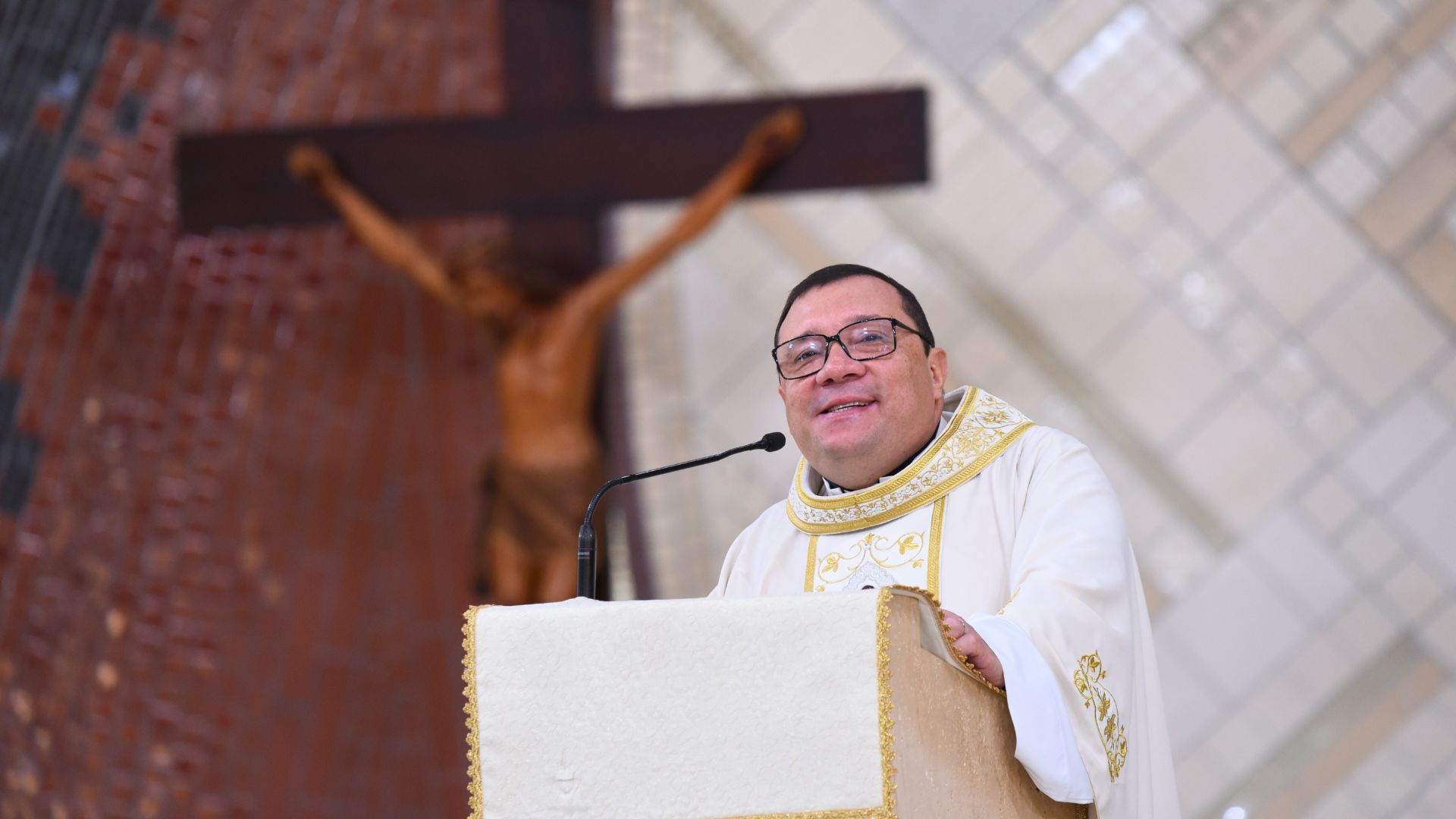 Padre Wagner Ferreira no ambão da palavra com cruz ao fundo, no santuário do Pai das Misericórdias
