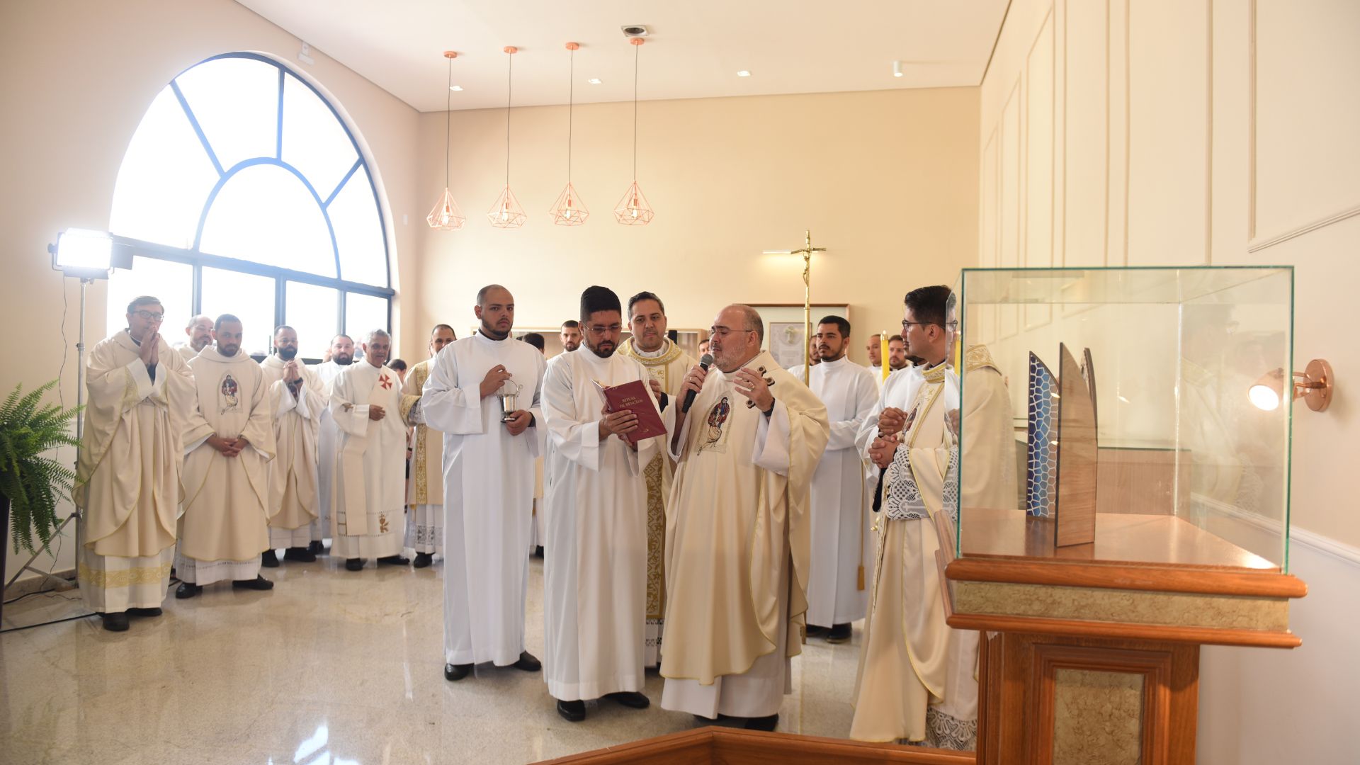 Padre faz oração de benção junto com outros sacerdotes dentro da nova sala das graças, luz ilumina