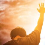 Entre a Vida e a Morte: A escolha que define sua Quaresma - Jovem com a mão levantanda ao alto céu com nuvens