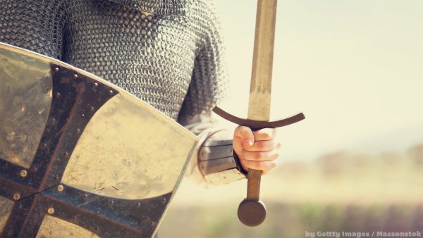 Nesta imagem temos um soldado com roupa medieval, segurando uma espada na mão esquerda e um escudo de ferro na mão direita. Pronto para o combate