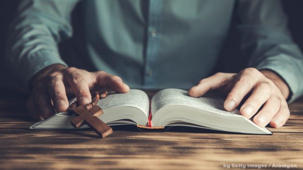 Pessoa lendo a bíblia com crucifixo sobre as páginas